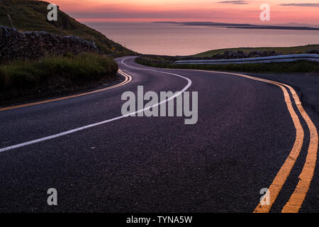 Sie suchen eine geschwungene Straße in der Nähe der Klippen von Moher zu schönen rosa Himmel Sonnenuntergang über der Insel Inisheer, niemand im Bild Stockfoto