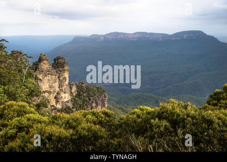 Zwei der drei Schwestern Felsformation in den Blue Mountains mit massiven Berg mit Orange im letzten Sonnenlicht, Katoomba, New South Wales, Australien Stockfoto