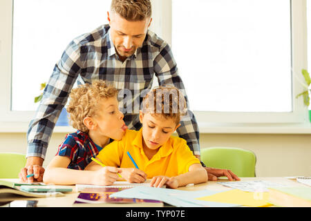 Schlechtes Verhalten. Schöne blonde Junge, der seine Zunge, während seine Mitschüler hänseln während der Lektion Stockfoto