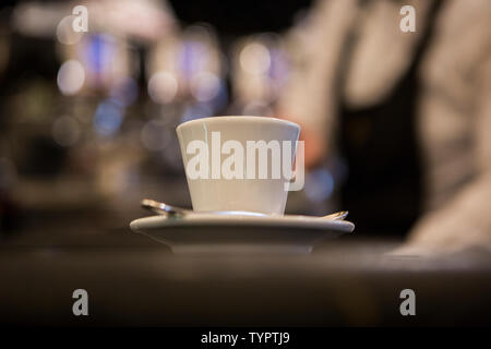 Weiße Tasse Espresso mit einem Löffel auf einer Tabelle in eine italienische Bar mit einem verschwommenen und funkelnden Hintergrund Stockfoto