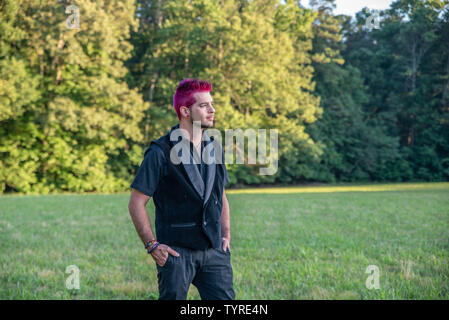 Alternative weiß kaukasischen Mann mit rosa Haaren außerhalb den Blick in die Ferne, nachdenklich. Bäume im Hintergrund mit Leeren leeren Raum Platz für Stockfoto