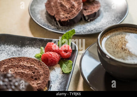 Schokolade schweizer Brötchen mit Marmelade mit Himbeeren auf einer Platte und einem schwarzen Kaffee auf den Tisch eingerichtet. Süßigkeiten. Selektive konzentrieren. Stockfoto