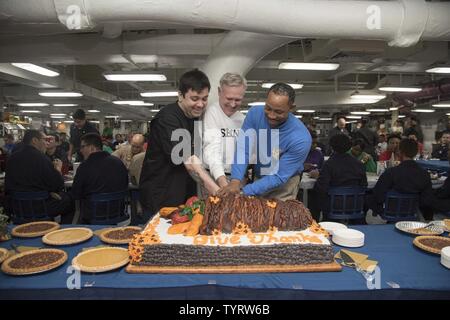 Golf (Nov. 24, 2016) der Sekretär der Marine Ray Mabus, Mitte, Petty Officer 1st Class Jonathan Ruiz, Links, und Command Master Chief Ty Blockton schnitt einen Kuchen bei einem Erntedankfest Besuch an Bord der Flugzeugträger USS Dwight D. Eisenhower (CVN 69) (IKE). Kulinarische Ike-Spezialisten mehr als 4.950 Pfund der Türkei, 1.050 Pfund Schinken, 1.200 Pfund Rinderfilet, 648 Pfund Shrimp Cocktail, 7.000 Teile von Kartoffelpüree, 400 Torten und 200 Käsekuchen für das Schiff Thanksgiving Mahlzeit. Ike und Ihre Carrier strike Group sind zur Unterstützung der Operation inhärenten Lösen eingesetzt, Mar Stockfoto