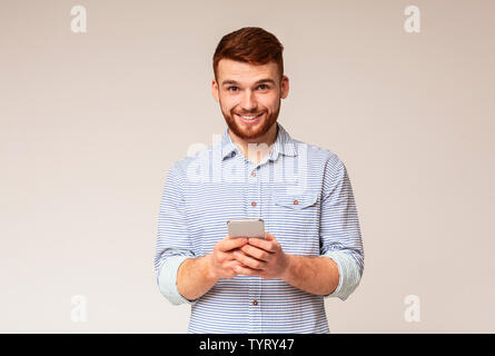 Junger bärtiger Mann mit seinem Telefon und lächelnd Stockfoto