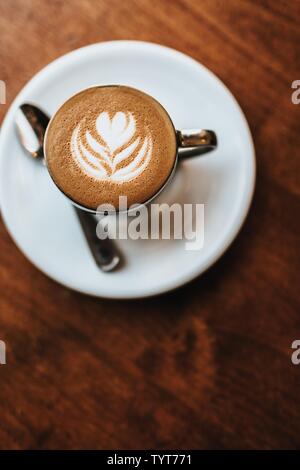 Wunderschön gemachtes Cappuccino mit Blumenkunst auf dem Schaum serviert Aufnahme aus der Ansicht von oben Stockfoto