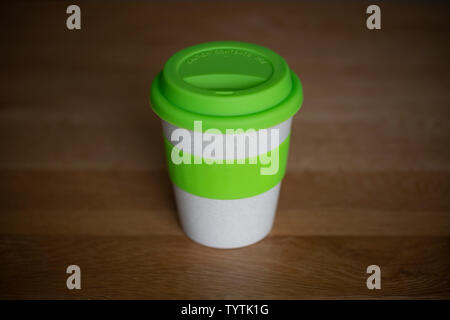 Eine isolierte wiederverwendbare Kaffeetasse sitzt auf einem Holztisch. Stockfoto