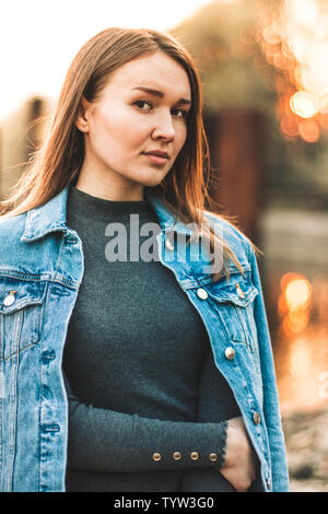 Portrait der Attraktive, schlanke, schöne junge Kaukasier blondes Mädchen in einer Jeans Jacke. Lächelnde Mädchen schönen warmen sunner Wetter gegen die Stockfoto