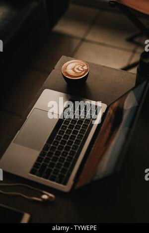 High-Angle-Aufnahme eines Laptops mit einem wunderschön gemachten Cappuccino mit Blumenkunst an der Seite Stockfoto