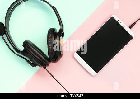 Schwarz Kopfhörer und Smartphone liegt auf einem farbenfrohen Pastelltönen rosa Hintergrund. Musik hören. Tragbare Technologie. Flach Top View Stockfoto
