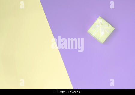 Kleiner gelber Geschenkbox liegen auf Textur Hintergrund der Mode pastell Gelb und Violett Farben Papier in minimalen Begriff. Stockfoto