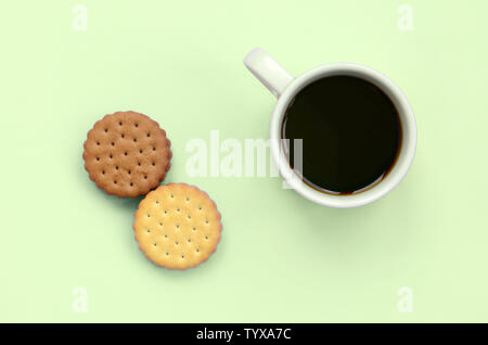 Kaffeepause flach Zusammensetzung mit braunen sandwich Cookies. Weiße heiße Tasse Kaffee und braun Dessert auf einem trendigen Pastellfarben Kalk Hintergrund Stockfoto