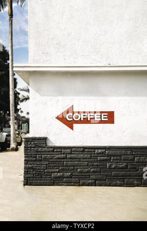 Rotes Pfeilschild auf einem weißen Gebäude mit einer Schrift „KAFFEE“ darauf Stockfoto