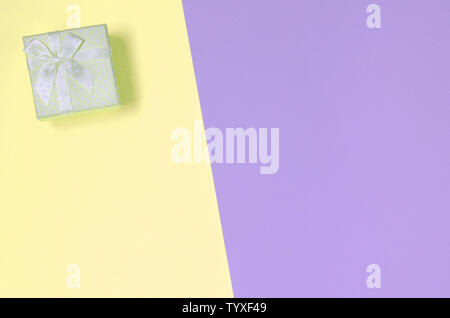 Kleiner gelber Geschenkbox liegen auf Textur Hintergrund der Mode pastell Gelb und Violett Farben Papier in minimalen Begriff. Stockfoto