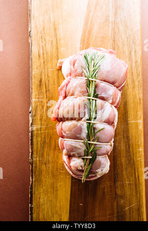 Raw roastbeef Fleisch zubereitet, caparisoned mit Schwein caul Fett und Rosmarin auf eine cutboard, Ansicht von oben oer einer braunen Hintergrund Stockfoto