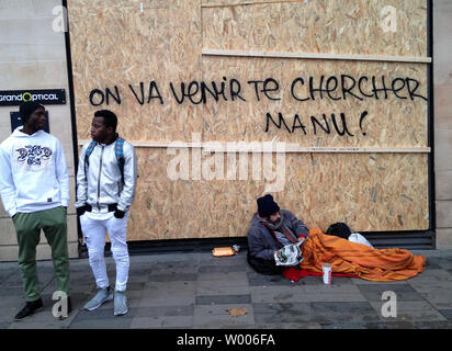 Ein obdachloser Mann liegt unter dem Fenster eines Store shuttered mit Holzbrettern und Lager ein Graffiti, das liest "Manu Wir kommen Sie in Bezug auf die Französische Präsident Emmanuel Längestrich, in Paris am 8. Dezember 2018. Gewalt brach mit Sicherheitskräften nach mehr als 30.000 "gelbe Weste' Demonstranten in den Straßen der Hauptstadt. Foto von Eco Clement/UPI Stockfoto
