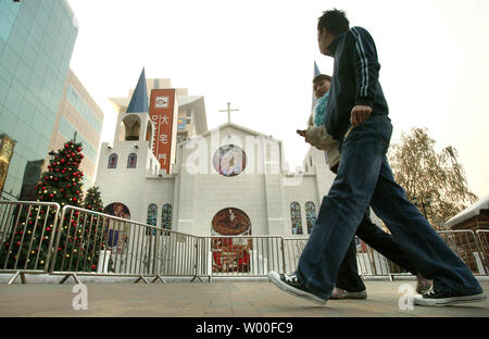 Ein Chinesisches paar Wanderungen vorbei an einem kleinen Modell Kirche als Teil eines Weihnachten Anzeige vor einem trendigen Büro- und Einkaufszentrum in der Innenstadt von Peking, China, November 04, 2006. Der Vatikan am Samstag sprengte China für Ordination einen anderen Bischof ohne päpstliche Zustimmung für sich, und nannte es die neuesten in einer 'Serie von sehr schwere Handlungen", die Papst Benedikt XVI." großes Leid verursacht." (UPI Foto/Stephen Rasierer) Stockfoto