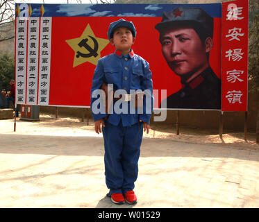 Ein chinesischer Junge in eine kommunistische Uniform gekleidet posiert für ein Foto vor einem Banner der ideale Soldat Li Feng der kommunistischen Partei, die an einem Standort durch ehemalige Steuermann Mao Zedong und anderen Führern verwendet Politik und zukünftige Strategien in der Yangjialing Revolution zu diskutieren, in Yan'an, Provinz Shaanxi, am 6. April 2014. Yan'an war in der Nähe der Endpunkt der Langen Marsch, und wurde zum Zentrum der Chinesischen Kommunistischen Revolution führte meine Mao von 1936 bis 1948. Die chinesischen Kommunisten feiern die Stadt als Geburtsstätte des modernen China und der Kult von Mao. UPI/Stephen Rasierer Stockfoto