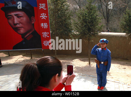 Ein chinesischer Junge in eine kommunistische Uniform gekleidet posiert für ein Foto vor einem Banner der kommunistischen Partei ist ideal Soldat Li Feng (L), an einem Standort durch ehemalige Steuermann Mao Zedong und anderen Führern verwendet Politik und zukünftige Strategien in der Yangjialing Revolution zu diskutieren, in Yan'an, Provinz Shaanxi, am 6. April 2014. Yan'an war in der Nähe der Endpunkt der Langen Marsch, und wurde zum Zentrum der Chinesischen Kommunistischen Revolution führte meine Mao von 1936 bis 1948. Die chinesischen Kommunisten feiern die Stadt als Geburtsstätte des modernen China und der Kult von Mao. UPI/Stephen Rasierer Stockfoto