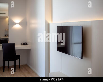 Schwarze LED-Fernseher auf weiße Wand in der Nähe von Make-up-Ecke mit schwarzem Stuhl vor dem Spiegel im Hotel Zimmer. Stockfoto