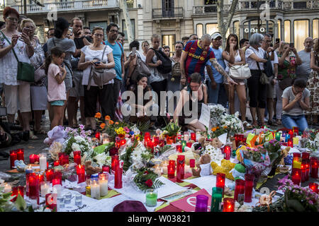Menschen stehen neben Blumen, Kerzen und andere Gegenstände auf die Font de Canaletes in Barcelona, als Sie erinnert an die Opfer des Barcelona Terroranschlag bezahlen, einen Tag nach dem van in die Menge gepflügt, tötete 14 Menschen und über 100 wurden verletzt, am 18. August 2017. Foto von Angel Garcia/UPI Stockfoto