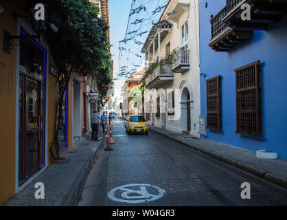 Ein Auto rollt eine Straße in der Altstadt von Cartagena de Indias, Kolumbien, gesäumt mit hellen, bunten Häusern. Stockfoto