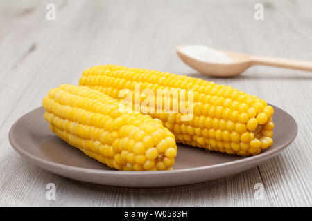 Maiskolben von gekochtem Mais auf braun Porzellan Teller und Löffel aus Holz mit Salz auf grauem Hintergrund. Stockfoto