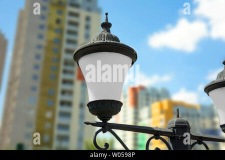 Gusseisernen Straßenlaternen auf unscharfen Hintergrund mit modernen bunten Gebäude entfernt. Closeup Bild in Tag Zeit auf blauen Himmel Stockfoto