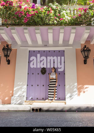 Mädchen steht vor einem bunten große Tür in der Altstadt von Cartagena de Indias, Kolumbien. Stockfoto