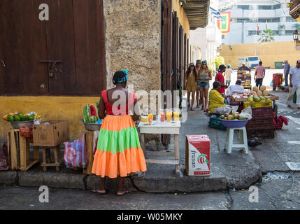 Eine Frau in einer bunten, hellen Kleid verkauft Obst an einer Straße stehen auf den Straßen von Cartagena, Kolumbien, im historischen Zentrum (Centro). Stockfoto
