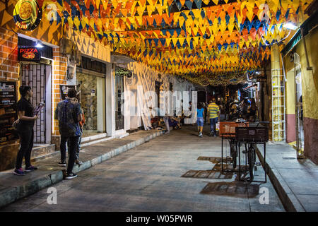 Strings der festlichen Fahnen schmücken die Straßen der Getsemani Nachbarschaft in der Nacht in Cartagena, Kolumbien, während Massen von Menschen hindurch gehen. Stockfoto