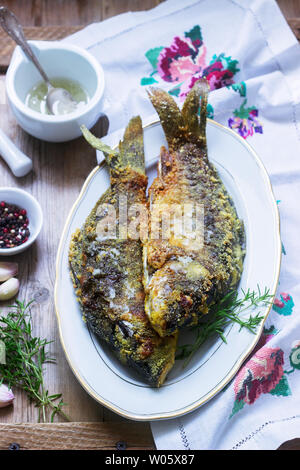 Traditionelle Moldauischen oder rumänischen Gericht, gebratener Fisch im Mais vor dem Panieren mit Knoblauch Sauce serviert. Rustikaler Stil, selektiven Fokus. Stockfoto