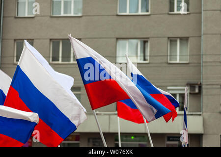 Eine große Anzahl von russischen Flaggen in tricolor mit Streifen in Weiß, Blau und Rot vor dem Hintergrund der Wände von Gebäuden mit grauen Windows dur Stockfoto