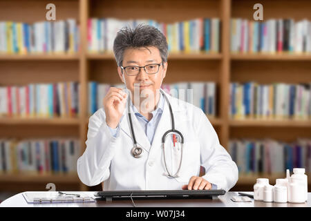 Asiatische männlicher Arzt am Schreibtisch sitzt lächelnd. Stockfoto