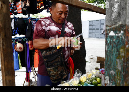 ANTIPOLO CITY, Philippinen - 25. JUNI 2019: eine Frucht Anbieter Schalen und Schichten eine indische Mango, die er auf seine Frucht Warenkorb verkauft. Stockfoto