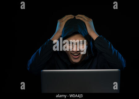 Erfolgreiche männliche Hacker posiert vor der Laptop, ballt Fäuste, in Schwarz gekleidet, freut sich Finishing fehlerhafte Daten Virus, Stockfoto