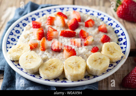 Haferflocken Porridge mit Erdbeeren und Bananen auf Holz rustikal Tisch. Gesundes Frühstück mit frischen Bio Beeren. Stockfoto