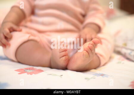 Kleines Baby sitzen. Nahaufnahme Bild von baby Bein und Fuß. gesundes und glückliches Kind sitzen auf ihren Selbst. Kleinkind setzte sich auf Bett. Frohes neues Familie Konzepte. Stockfoto