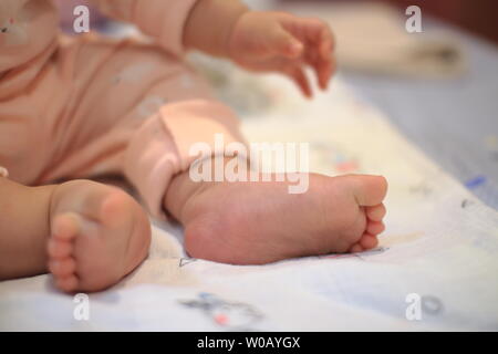 Kleines Baby sitzen. Nahaufnahme Bild von baby Bein und Fuß. gesundes und glückliches Kind sitzen auf ihren Selbst. Kleinkind setzte sich auf Bett. Frohes neues Familie Konzepte. Stockfoto