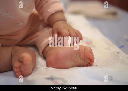 Kleines Baby sitzen. Nahaufnahme Bild von baby Bein und Fuß. gesundes und glückliches Kind sitzen auf ihren Selbst. Kleinkind setzte sich auf Bett. Frohes neues Familie Konzepte. Stockfoto