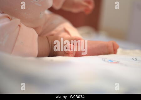 Kleines Baby sitzen. Nahaufnahme Bild von baby Bein und Fuß. gesundes und glückliches Kind sitzen auf ihren Selbst. Kleinkind setzte sich auf Bett. Frohes neues Familie Konzepte. Stockfoto