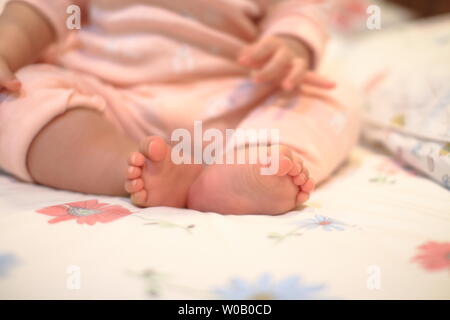 Kleines Baby sitzen. Nahaufnahme Bild von baby Bein und Fuß. gesundes und glückliches Kind sitzen auf ihren Selbst. Kleinkind setzte sich auf Bett. Frohes neues Familie Konzepte. Stockfoto