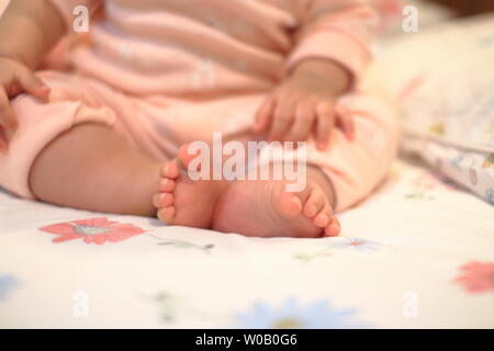 Kleines Baby sitzen. Nahaufnahme Bild von baby Bein und Fuß. gesundes und glückliches Kind sitzen auf ihren Selbst. Kleinkind setzte sich auf Bett. Frohes neues Familie Konzepte. Stockfoto