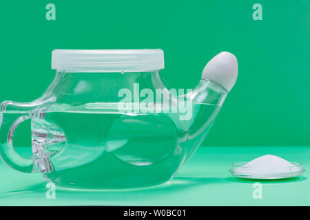 Neti Pot mit Soft Comfort Tipp und Haufen von Kochsalzlösung (Natriumbikarbonat und Natriumchlorid) auf grünem Hintergrund. Sinus waschen. Nasale Bewässerung. Stockfoto