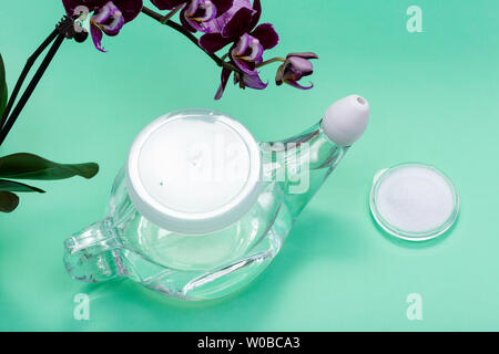 Neti Pot mit Soft Comfort Tipp, den Stapel der Saline und lila Orchidee Blumen auf grünem Hintergrund. Sinus waschen. Nasale Bewässerung. Stockfoto