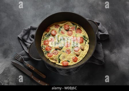 Frittata aus Eier, Pilze, Tomaten und Spinat in einer Pfanne serviert. Italienische Küche Stockfoto