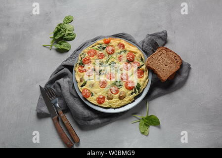 Frittata aus Eier, Pilze, Tomaten und Spinat auf einem Teller serviert. Italienische Küche Stockfoto