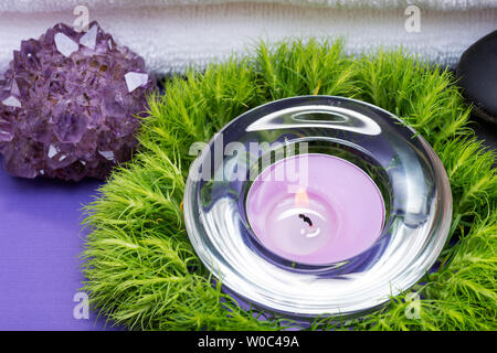 Wellness Entspannen Sie Konzept mit Spa Elemente. Weiße Handtücher, Basaltsteine, Lavendel Tee Kerze, Dianthus Blumen und Amethyst auf lila Hintergrund. Stockfoto