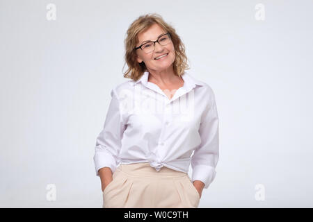Positive Frau mit Brille im mittleren Alter auf weißem Hintergrund posiert. Positive facial Emotion. Erfolgreiche Unternehmer und Karriere Konzept Stockfoto
