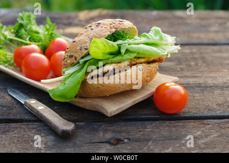 Leckere hausgemachte Burger und Salat, Tomaten auf hölzernen Tisch für Picknick im Freien. Stockfoto