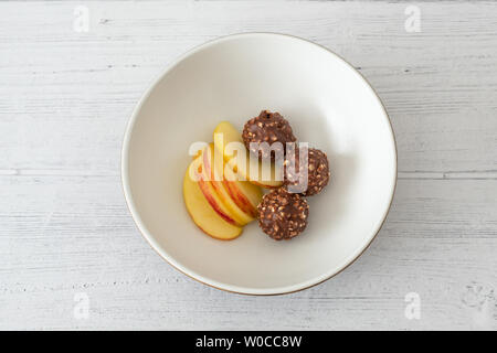 Eine Platte der Drei nussig Eis Kugeln und in Scheiben geschnittenen Apfel in einem weißen Servierschüssel sitzen auf einem weiß lackiertem Board. Stockfoto